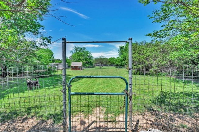 view of gate featuring a shed, a rural view, an outbuilding, a yard, and fence