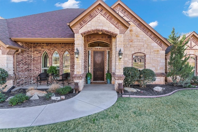 french provincial home with stone siding, a front lawn, brick siding, and roof with shingles