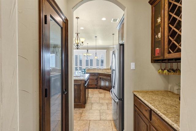 interior space with glass insert cabinets, arched walkways, light stone countertops, visible vents, and freestanding refrigerator