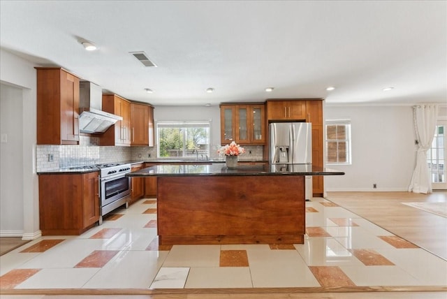 kitchen with stainless steel appliances, wall chimney range hood, a center island, brown cabinetry, and a sink