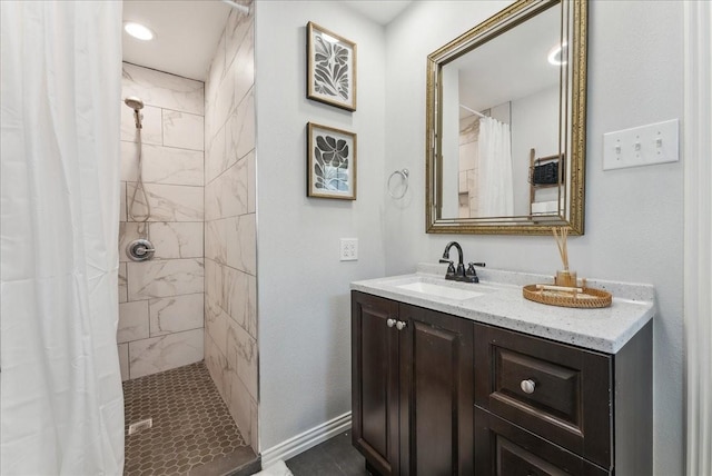 bathroom with a tile shower, vanity, and baseboards