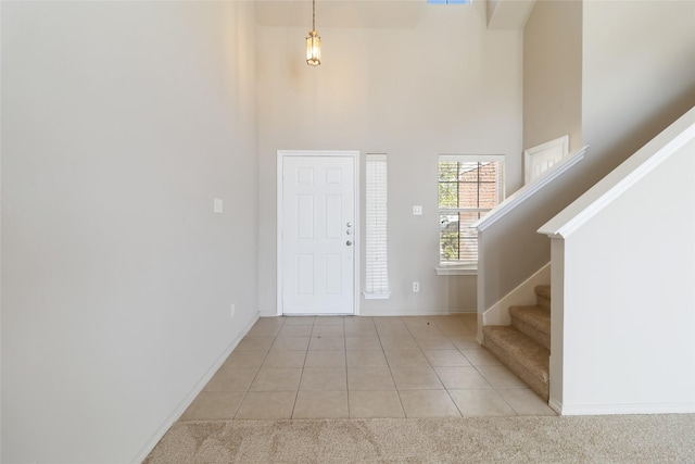 entrance foyer featuring light tile patterned floors, baseboards, a high ceiling, stairway, and light carpet