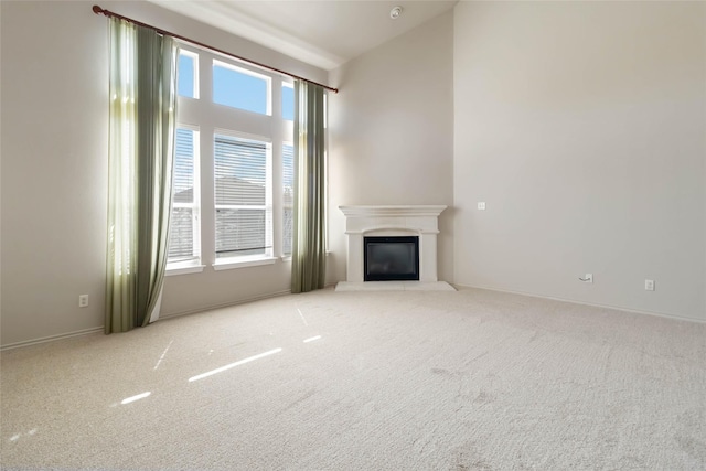 unfurnished living room with light carpet, baseboards, and a glass covered fireplace