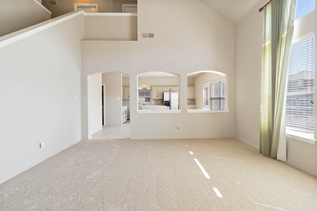 unfurnished living room featuring light carpet, plenty of natural light, high vaulted ceiling, and visible vents