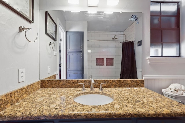 full bath featuring a shower with shower curtain, vanity, and wainscoting
