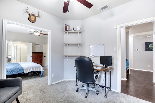 carpeted home office featuring baseboards, ceiling fan, visible vents, and wood finished floors