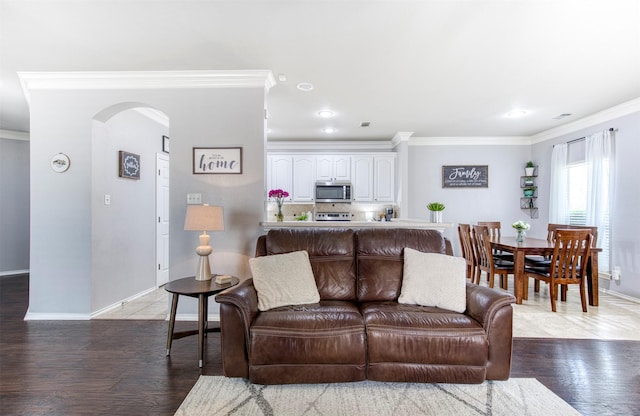 living area with arched walkways, baseboards, ornamental molding, and wood finished floors