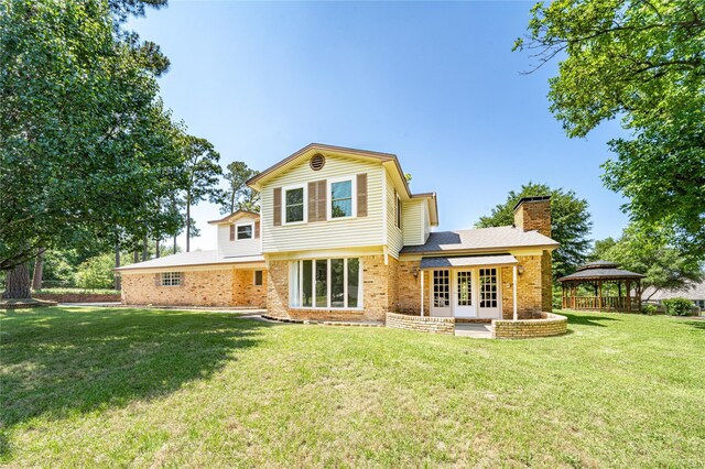 back of property featuring french doors, a gazebo, a chimney, brick siding, and a lawn