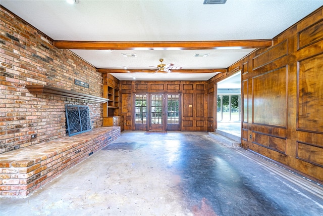 unfurnished living room featuring a fireplace, wood walls, beam ceiling, and a textured ceiling