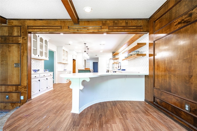 kitchen with light countertops, open shelves, wood finished floors, a peninsula, and glass insert cabinets