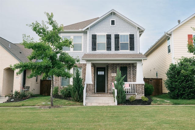 craftsman-style house with brick siding, a porch, a front yard, and a shingled roof