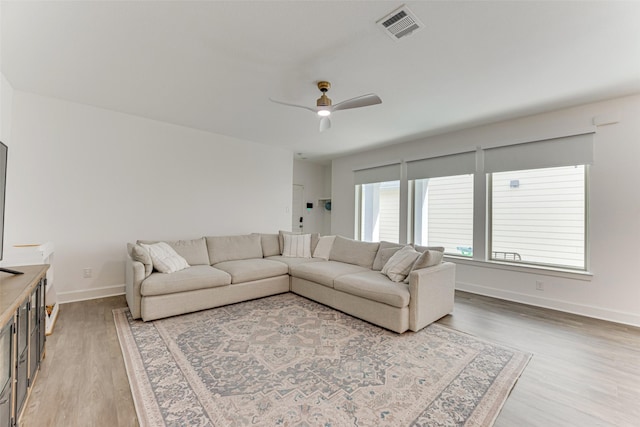 living area with light wood-style floors, a ceiling fan, and baseboards