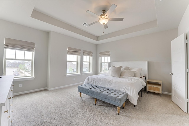 bedroom with light colored carpet, multiple windows, a tray ceiling, and baseboards