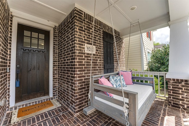 doorway to property featuring covered porch and brick siding