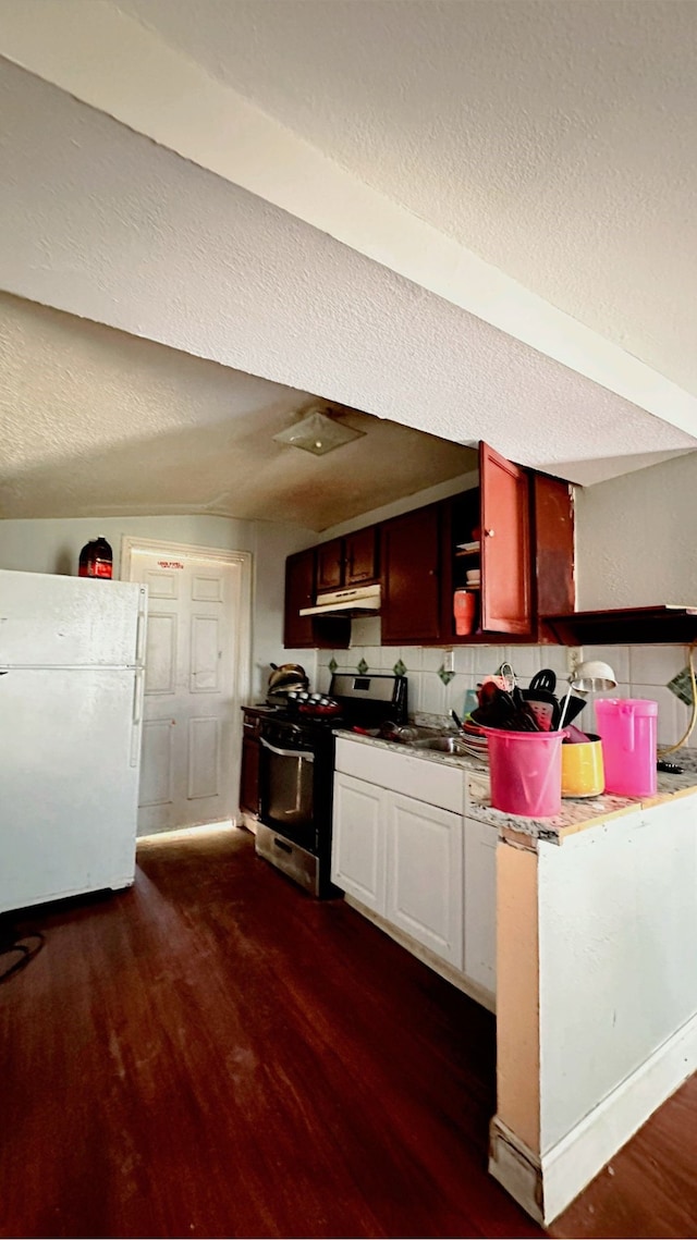 kitchen with dark wood finished floors, under cabinet range hood, gas range, backsplash, and freestanding refrigerator