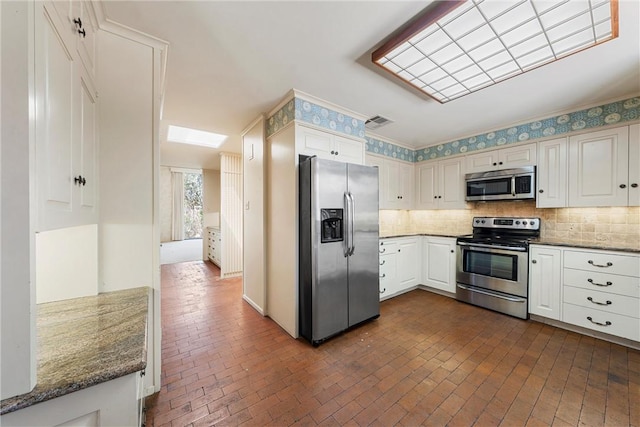 kitchen with tasteful backsplash, appliances with stainless steel finishes, brick floor, visible vents, and dark stone counters