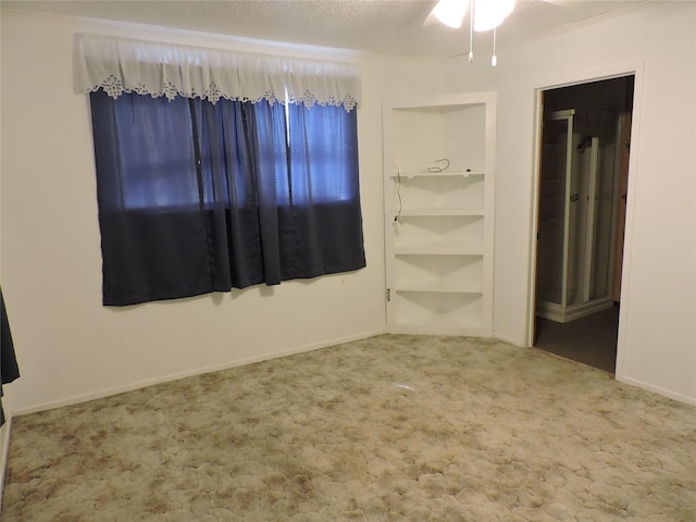 spare room featuring built in features, baseboards, a ceiling fan, a textured ceiling, and carpet flooring
