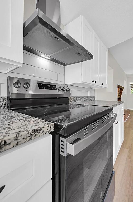 1541 Clark Ave, Waco, TX 76708 - kitchen featuring wall chimney range hood, white cabinetry, light wood finished floors, and electric stove