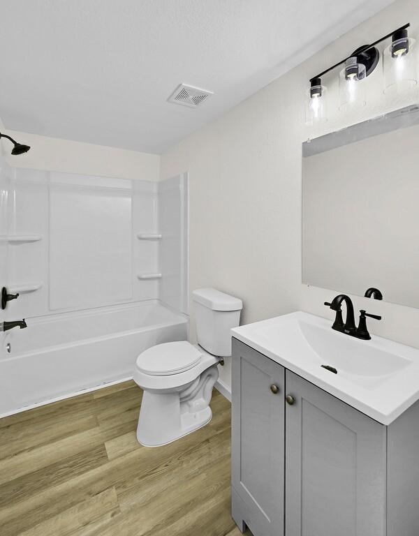 1541 Clark Ave, Waco, TX 76708 - bathroom featuring visible vents, toilet, wood finished floors, vanity, and shower / bath combination