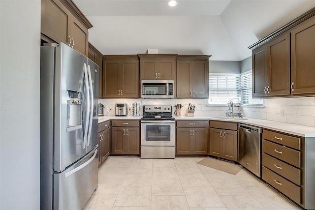 kitchen featuring light countertops, a sink, lofted ceiling, stainless steel appliances, and decorative backsplash