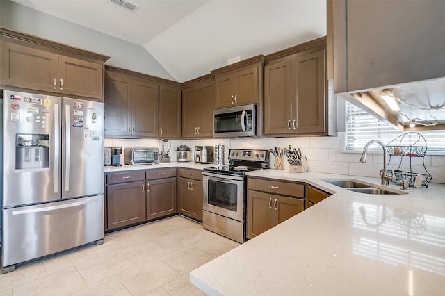 kitchen featuring visible vents, stainless steel appliances, tasteful backsplash, lofted ceiling, and a sink