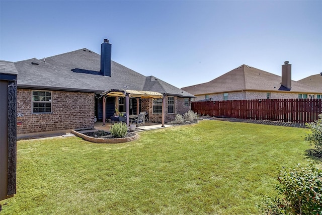 back of property featuring a chimney, fence, brick siding, a patio, and a lawn