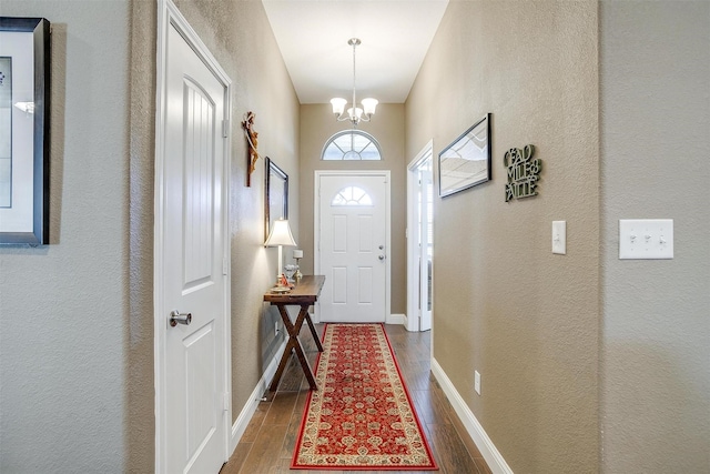 entryway with baseboards, a textured wall, wood finished floors, and a notable chandelier