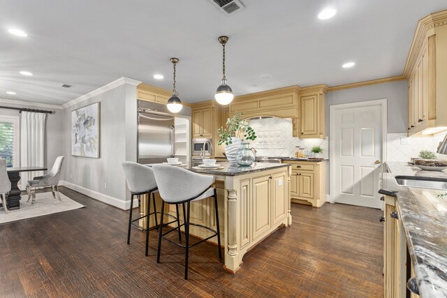 kitchen with a sink, cream cabinets, a center island with sink, decorative backsplash, and stainless steel range
