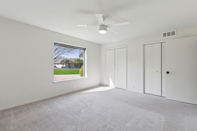 unfurnished bedroom with visible vents, two closets, carpet flooring, and a ceiling fan