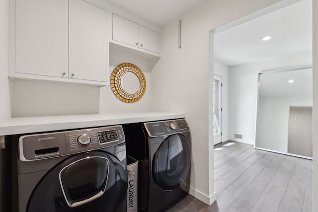 washroom featuring wood finished floors, washing machine and clothes dryer, baseboards, visible vents, and cabinet space