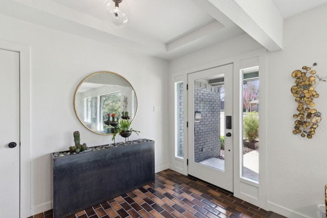 entryway featuring baseboards, brick floor, a tray ceiling, and plenty of natural light