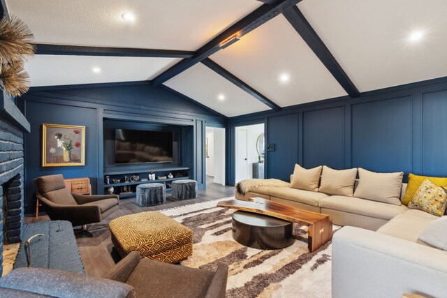 home theater room with lofted ceiling with beams, wood finished floors, a decorative wall, and a fireplace