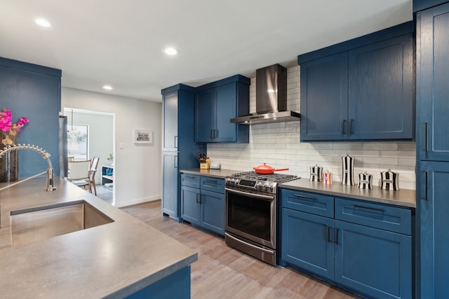 kitchen featuring stainless steel range with gas stovetop, blue cabinets, backsplash, a sink, and wall chimney range hood