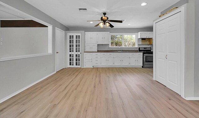 kitchen with stainless steel range with gas cooktop, dark countertops, light wood-type flooring, ceiling fan, and white cabinets