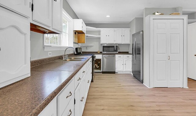 kitchen with white cabinets, stainless steel appliances, a sink, and dark countertops
