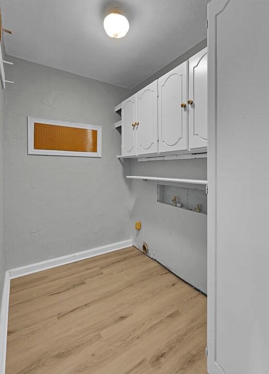 clothes washing area featuring light wood-style flooring, baseboards, washer hookup, and cabinet space