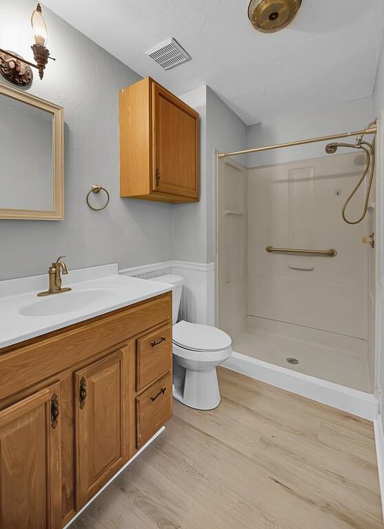 bathroom with wood finished floors, visible vents, toilet, vanity, and walk in shower