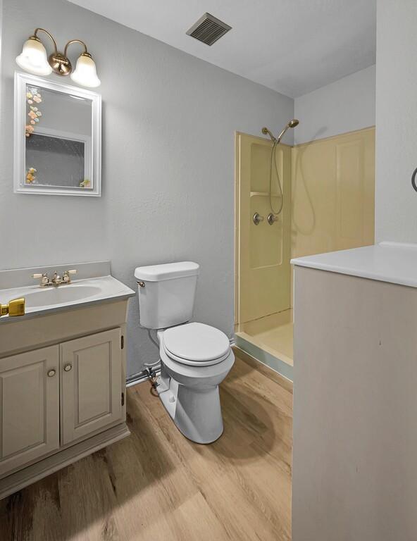 full bath with wood finished floors, vanity, walk in shower, toilet, and visible vents