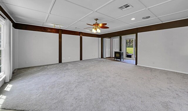 spare room featuring a wood stove, visible vents, carpet floors, baseboards, and ceiling fan