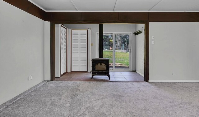 unfurnished room with carpet flooring, a wood stove, and tile patterned floors