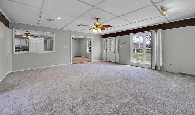 unfurnished living room featuring ceiling fan, a wealth of natural light, and carpet flooring