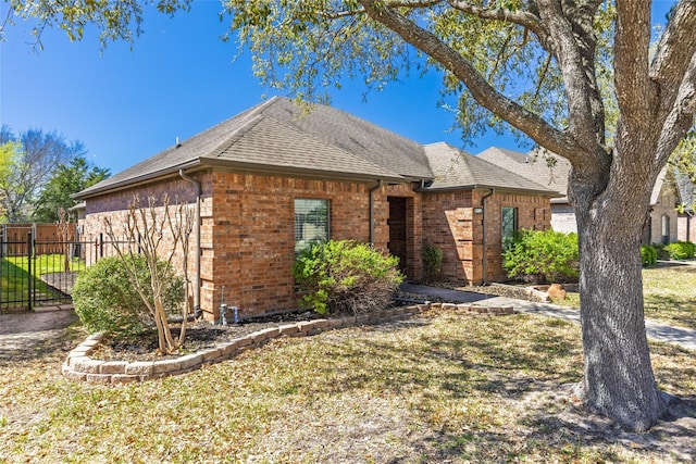 ranch-style home featuring a front lawn, a shingled roof, fence, and brick siding