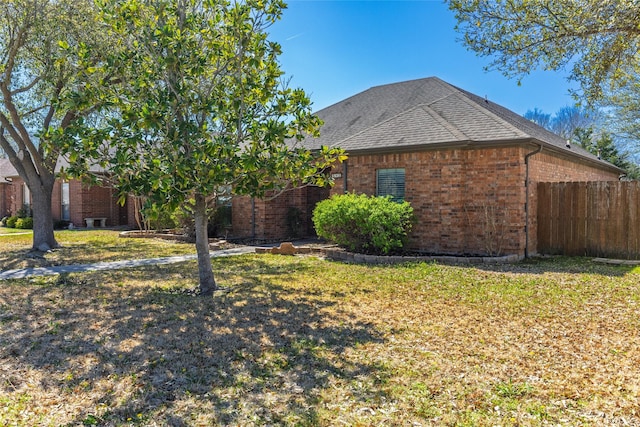 exterior space featuring a lawn, brick siding, fence, and roof with shingles
