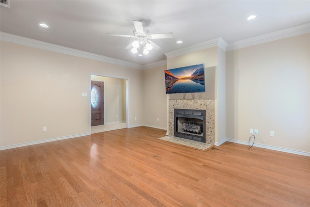 unfurnished living room with a tiled fireplace, ornamental molding, light wood-style floors, and ceiling fan