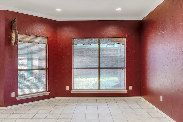 empty room with light tile patterned flooring, a textured wall, crown molding, and baseboards