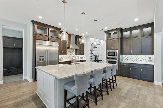 3905 Dashiell Dr, Flower Mound, TX 75022 - kitchen with wall chimney range hood, built in appliances, backsplash, light wood finished floors, and recessed lighting