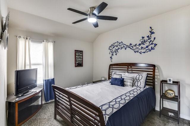 bedroom with baseboards, vaulted ceiling, carpet, and a ceiling fan