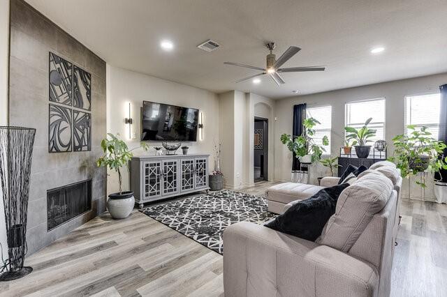 living room with a fireplace, ceiling fan, visible vents, and wood finished floors