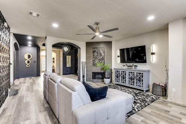 living room featuring visible vents, a tile fireplace, light wood finished floors, a ceiling fan, and arched walkways