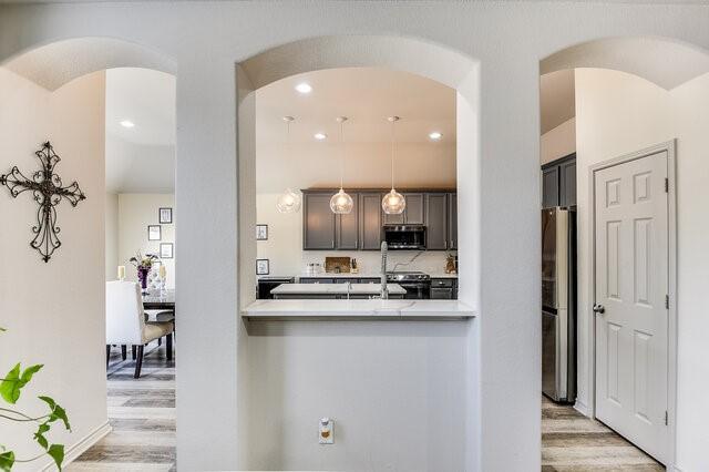 kitchen with arched walkways, light countertops, light wood-style flooring, and appliances with stainless steel finishes